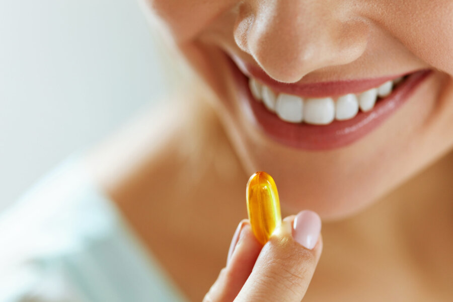 Vitamin And Supplement. Closeup Of Beautiful Young Woman Taking Yellow Fish Oil Pill. Female Hand Putting Omega-3 Capsule In Mouth. Healthy Eating And Diet Nutrition Concepts. High Resolution Image